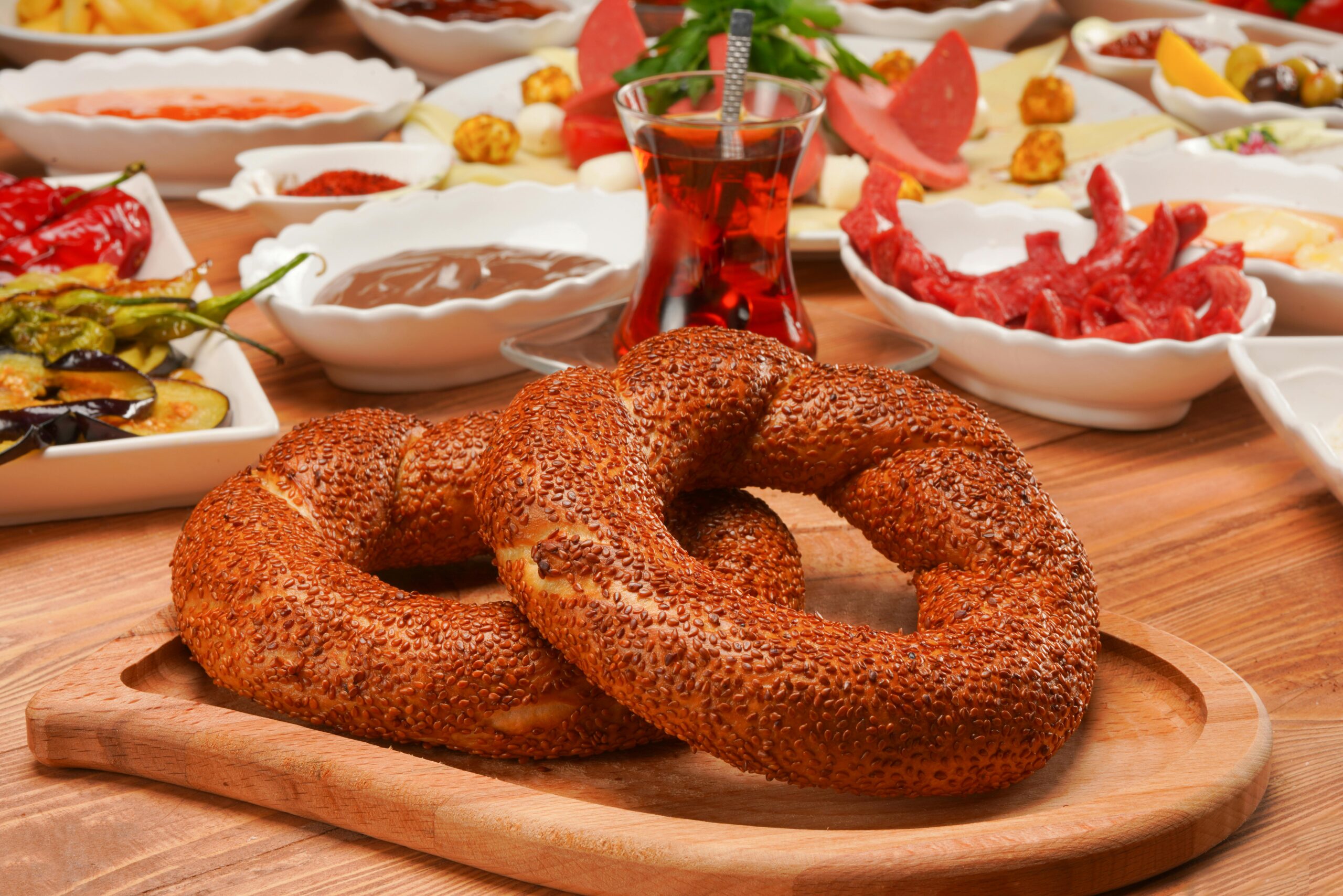Traditional Turkish breakfast spread featuring fresh sesame bagels and assorted dishes on a wooden surface.